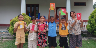 A row of happy children standing at the center, holding up artwork they've made