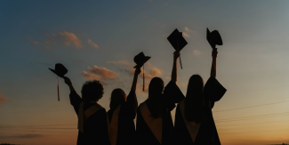 Image of students tossing their caps with a sunset behind them